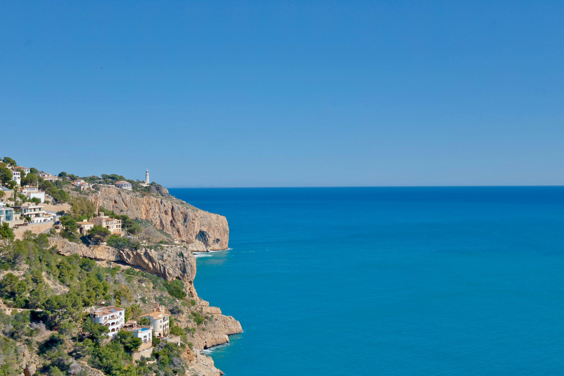 Panoramisch uitzicht op de rotsachtige kustlijn en de Middellandse Zee vanuit Jávea, met witte huizen op de heuvel.