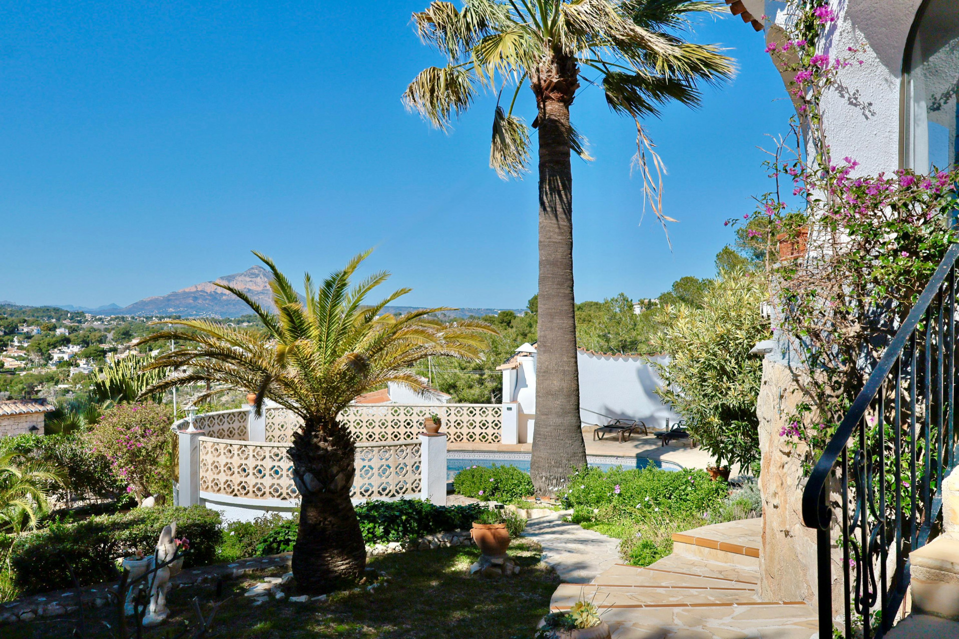 Tuin met zwembad en palmbomen, met nadruk op de mediterrane vegetatie en het berglandschap op de achtergrond.