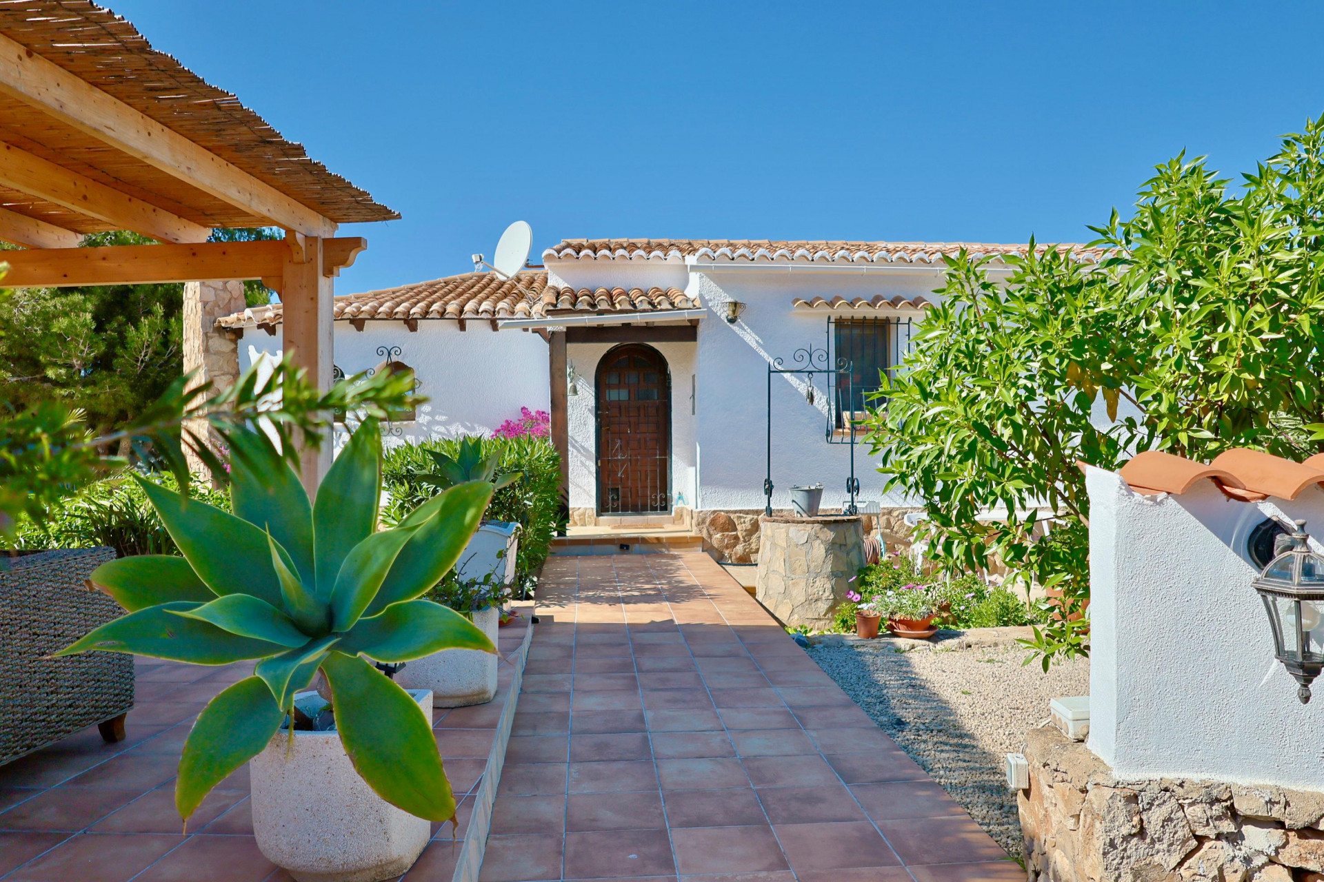 Villa-ingang met betegeld pad, mediterraan groen en een stenen waterput.