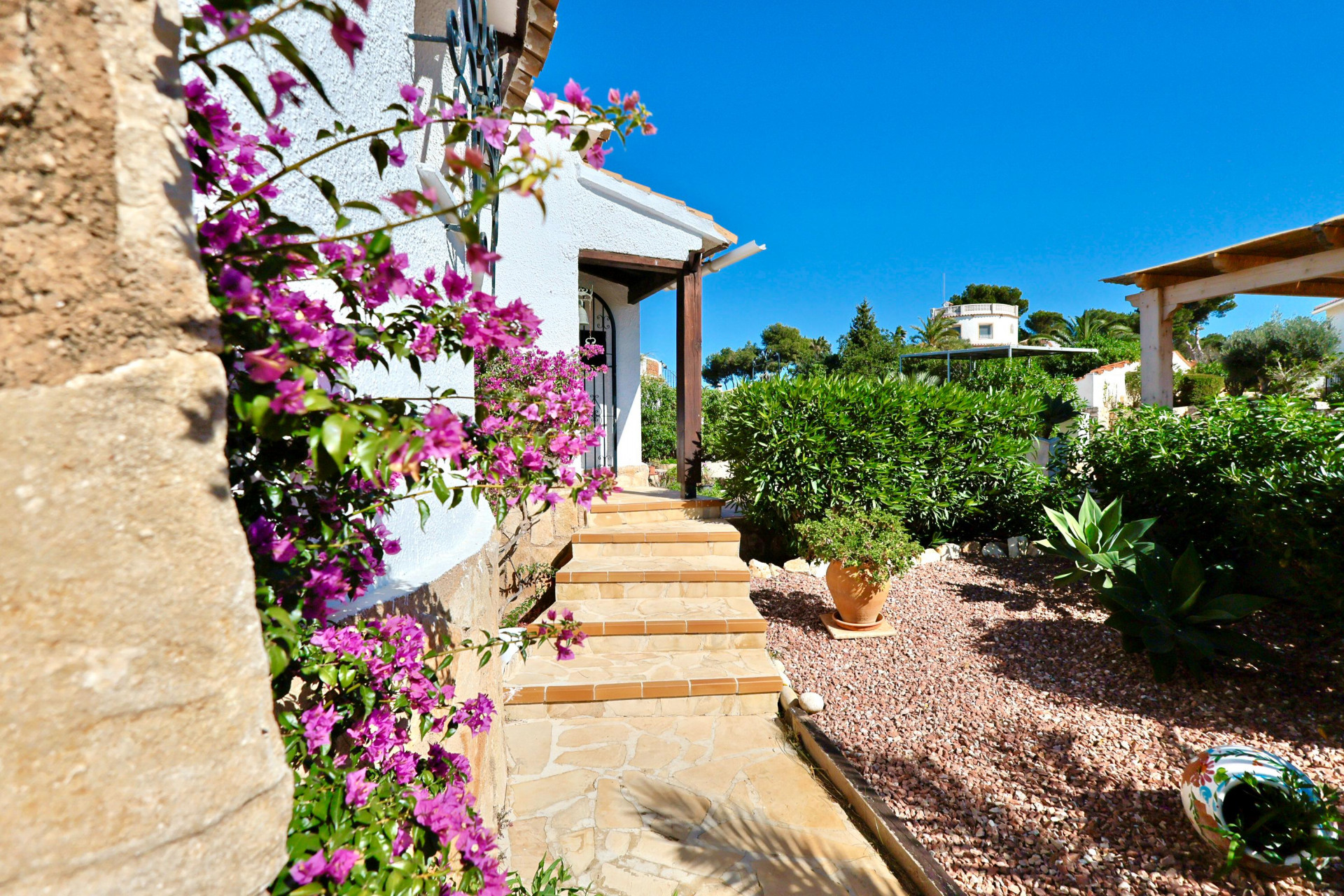 Villa-ingang met fuchsia bougainvillea en grindtuin.
