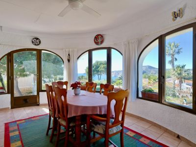 Lichte eetkamer met uitzicht op zee, omgeven door boogvensters en rustieke inrichting.