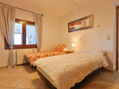 Lichte slaapkamer met twee eenpersoonsbedden, een houten raamkozijn en een tegelvloer.