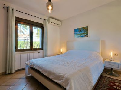 Lichte slaapkamer met tweepersoonsbed, moderne nachtkastjes en een raam met uitzicht naar buiten.