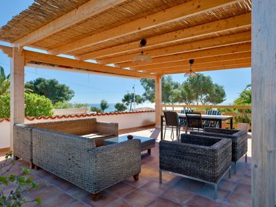 Overdekt terras met rotan meubilair en uitzicht op zee.
