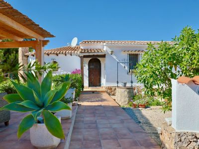Villa-ingang met betegeld pad, mediterraan groen en een stenen waterput.