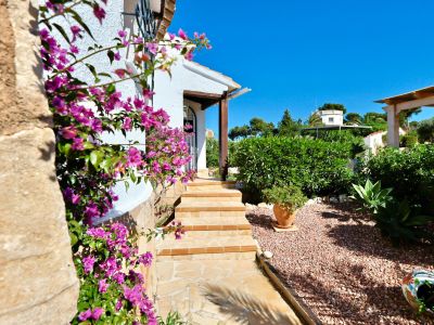 Villa-ingang met fuchsia bougainvillea en grindtuin.