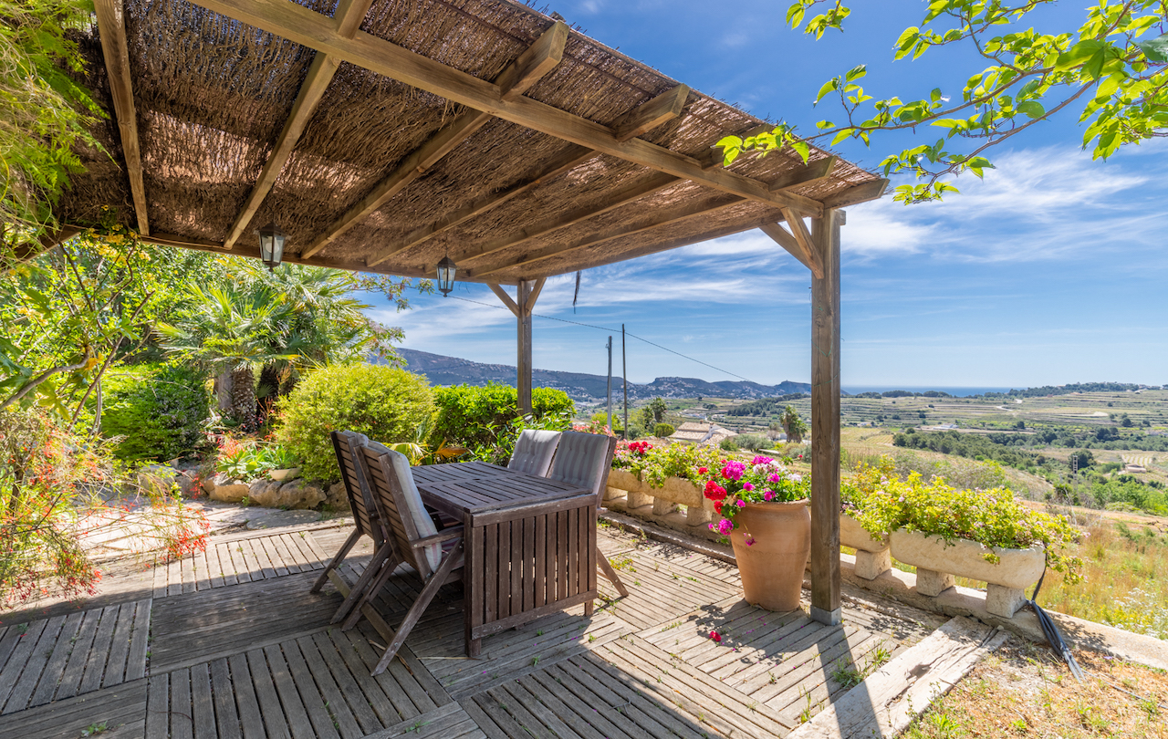 Buitenterras met houten pergola en heidematten, teakhouten eethoek en panoramisch uitzicht over de wijngaarden en de Middellandse Zee.