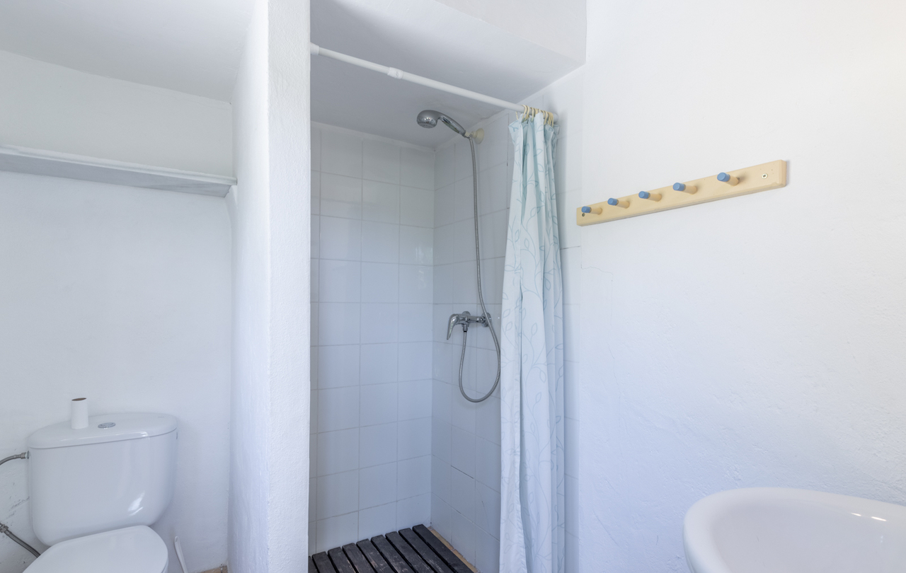 Functionele badkamer met betegelde inloopdouche, donkerhouten vlonder, gordijn met patroon en een houten wandkapstok met blauwe knoppen.