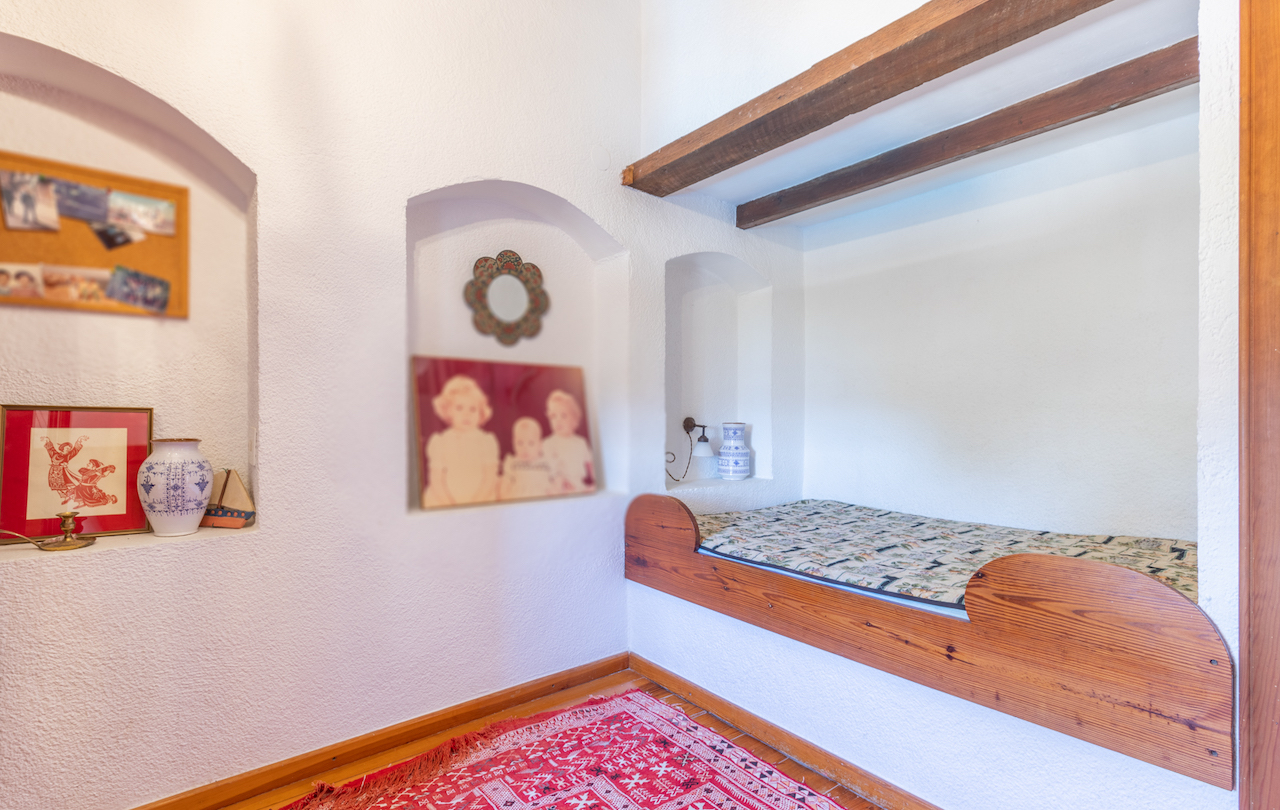 Rustieke slaapkamer met een ingebouwd houten alkoofbed, zichtbare balken en decoratieve muurnissen in traditionele witte muren.