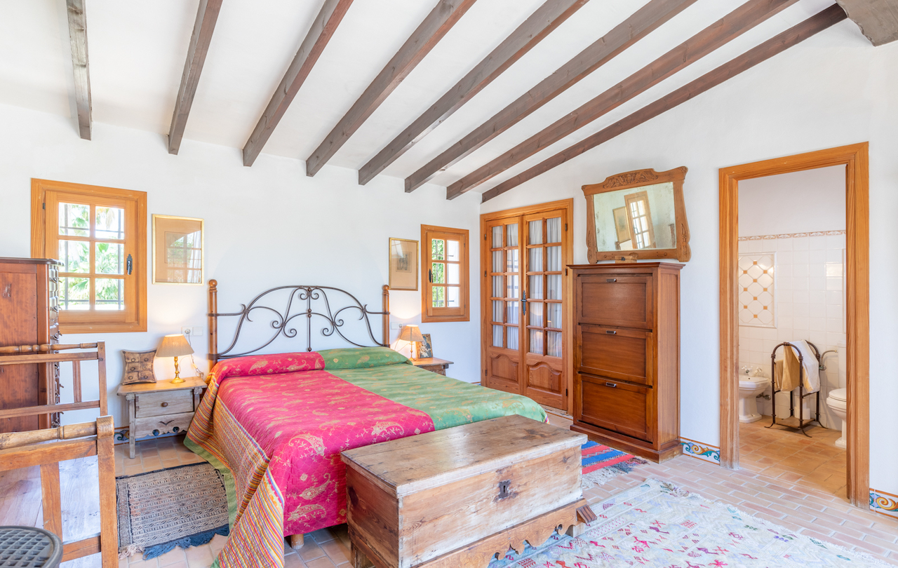 Rustieke slaapkamer met houten plafondbalken, terracotta vloertegels en traditioneel meubilair. De kamer heeft directe toegang tot een aangrenzende badkamer.