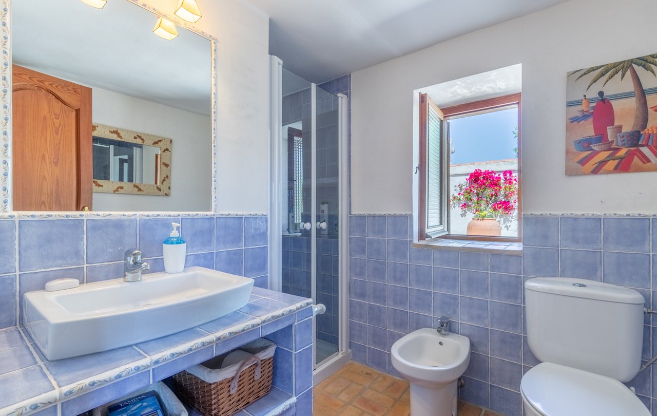 Traditionele badkamer met blauwe wandtegels, terracotta vloer en houten raam naar de patio. Voorzien van een opzetwastafel, bidet en een glazen douchecabine.