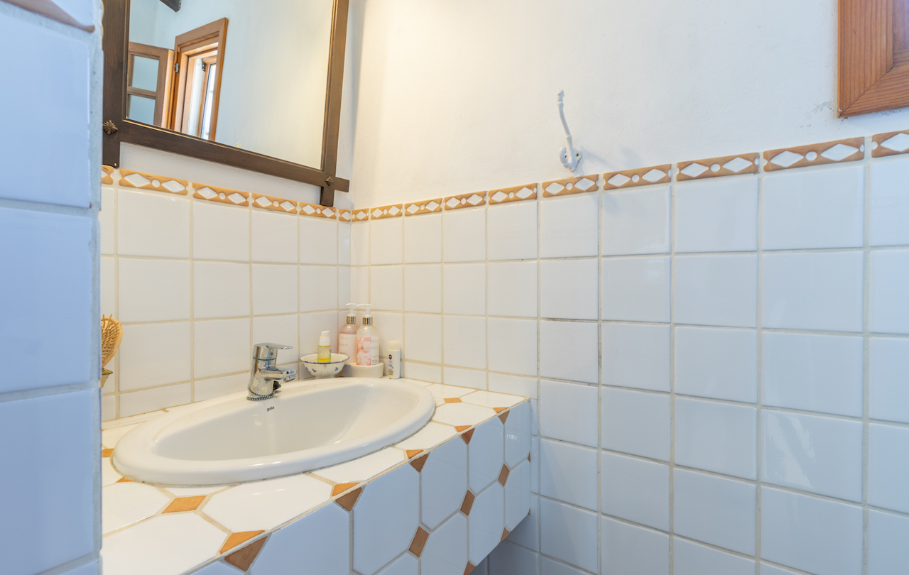Traditionele badkamer met witte tegels en een decoratieve rand. Voorzien van een inbouwwastafel op een betegeld blad met geometrische details en een spiegel met houten lijst.