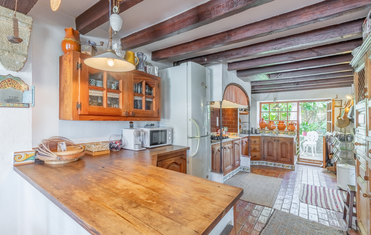 Traditionele keuken met zichtbare houten balken, massief houten werkbladen en directe toegang tot een groene patiotuin.