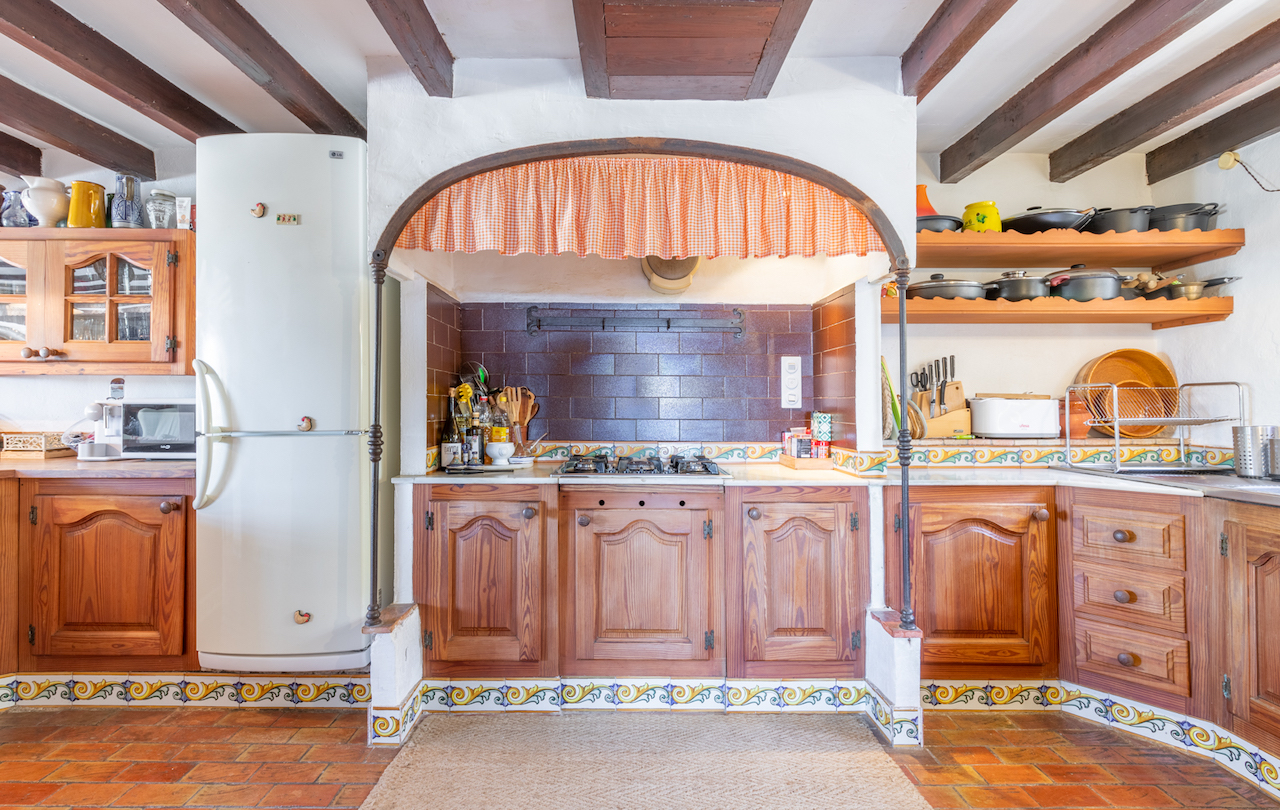 Traditionele Valenciaanse keuken met houten plafondbalken, terracotta vloertegels en een kookgedeelte onder een decoratieve boog met ambachtelijk tegelwerk.