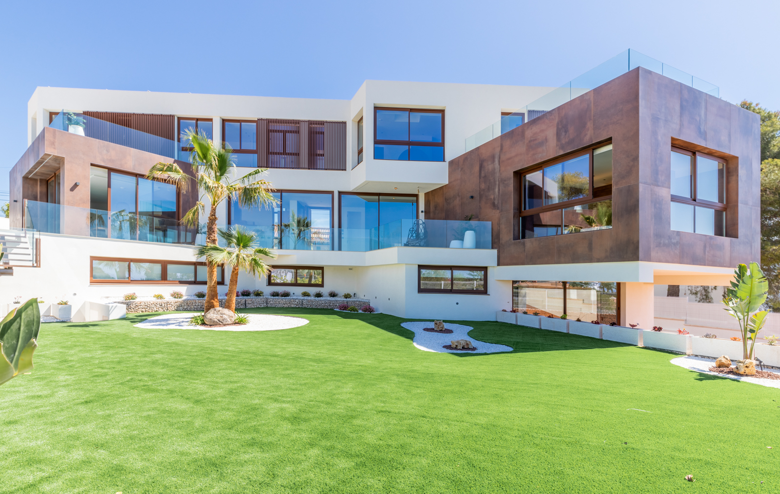 Buitenaanzicht van de villa met gazon, palmbomen en een moderne gevel met grote ramen.