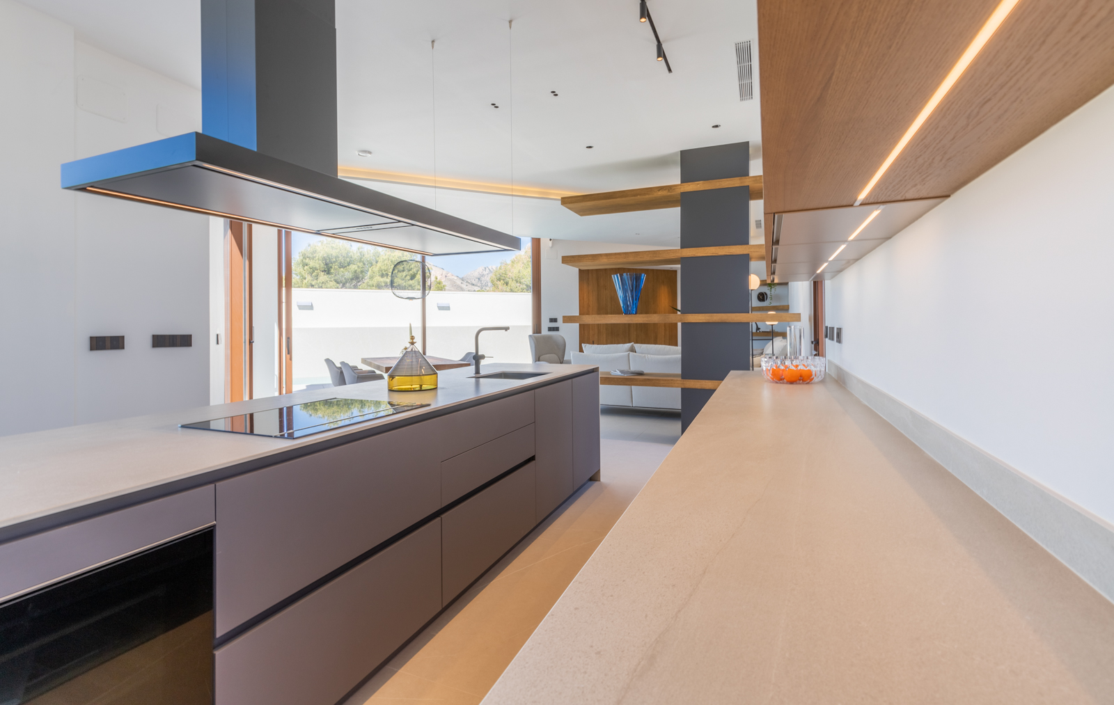 Detail van de moderne keuken met grijs eiland, beige aanrechtblad en verlichte houten planken.