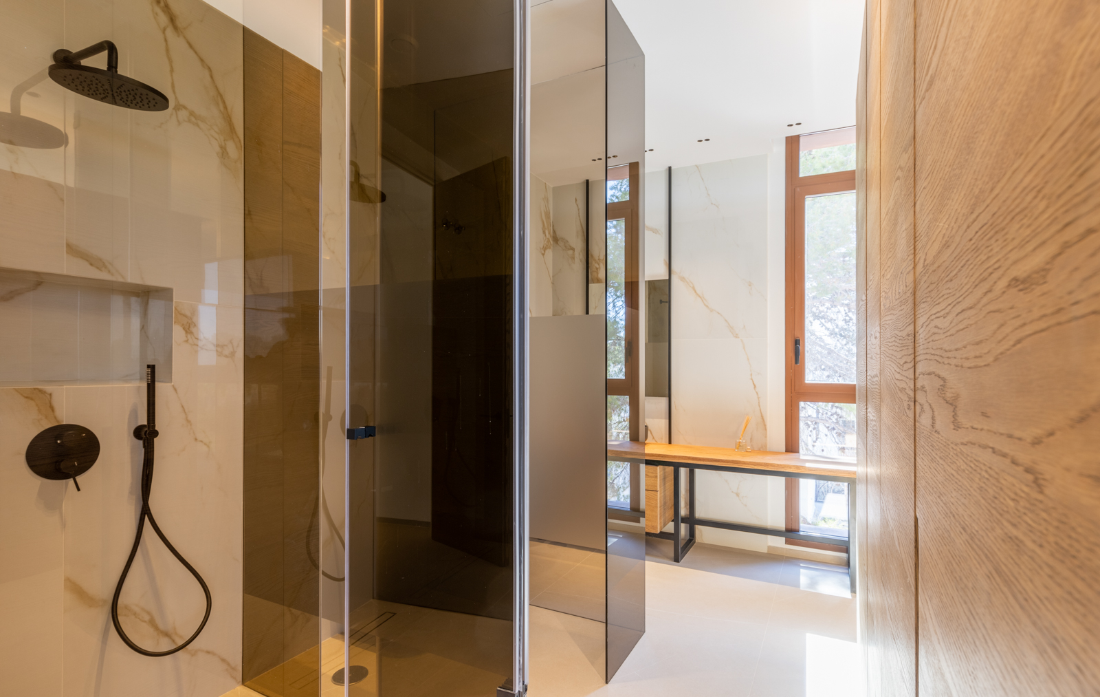 Douche detail met rookglas en licht houten wastafel in een moderne badkamer met geaderde tegels.