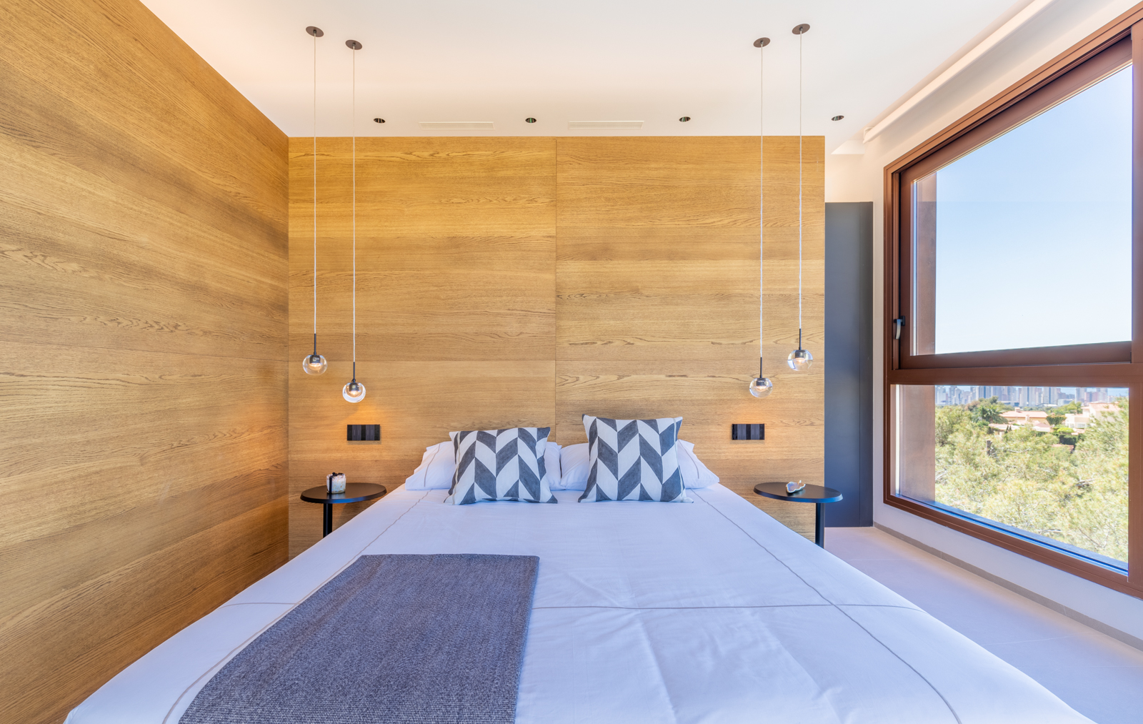 Slaapkamer met lichte houten wand, bolvormige hanglampen en uitzicht naar buiten.