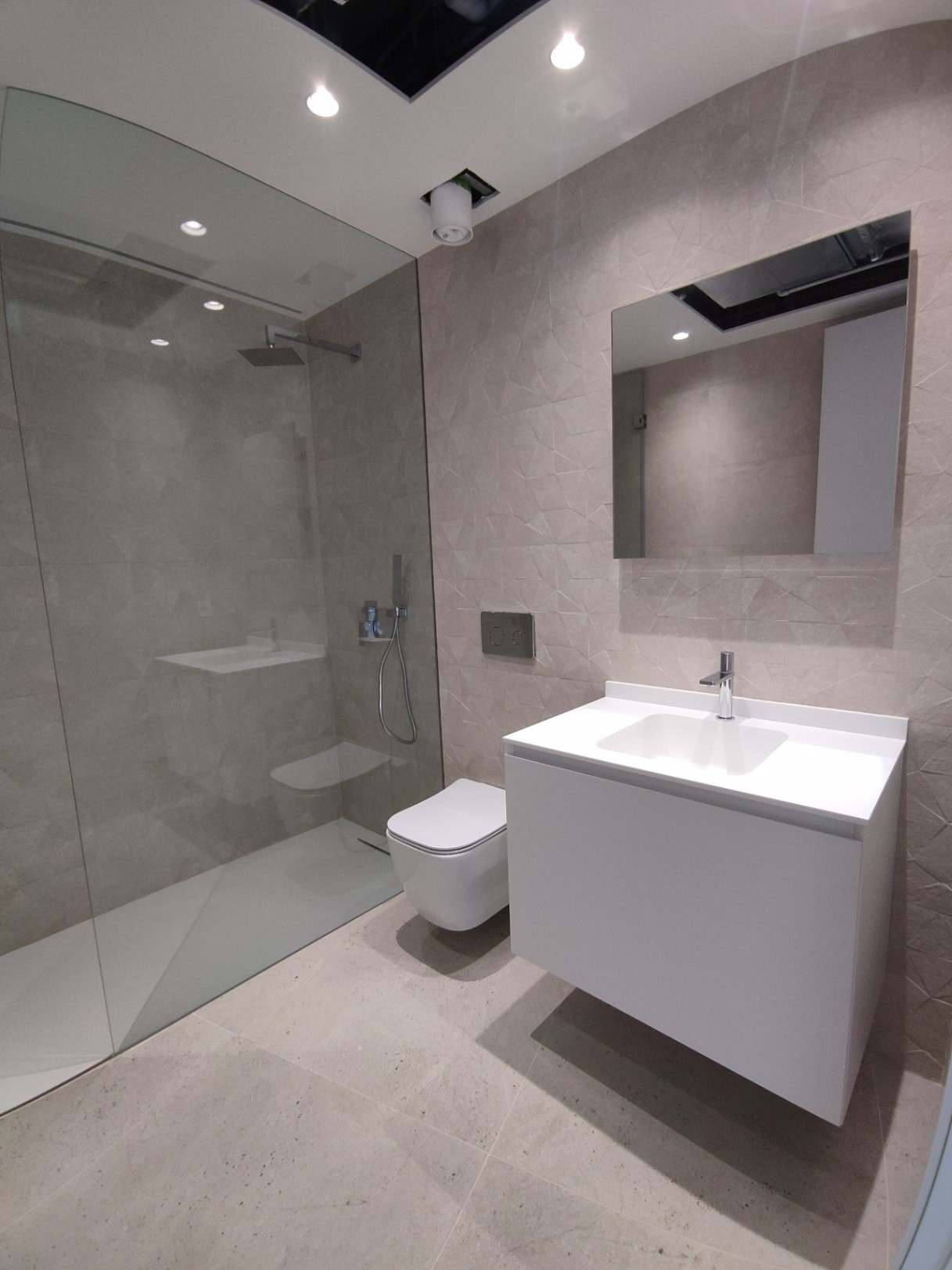 Moderne badkamer met glazen inloopdouche, hangend toilet en wit zwevend wastafelmeubel tegen een wand met geometrisch reliëf.
