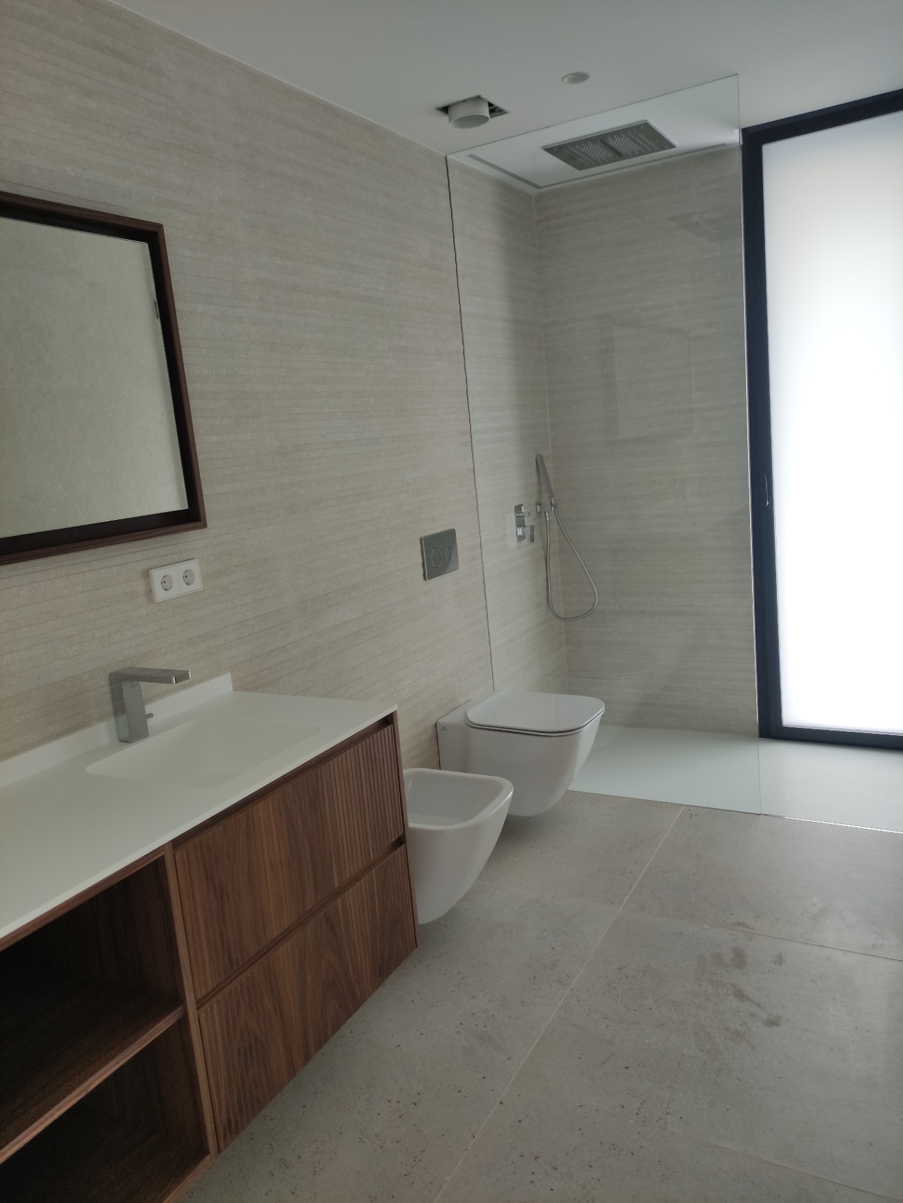 Moderne badkamer voorzien van een houten wastafelmeubel, hangend sanitair en een inloopdouche met plafonddouche en glazen scheidingswand.