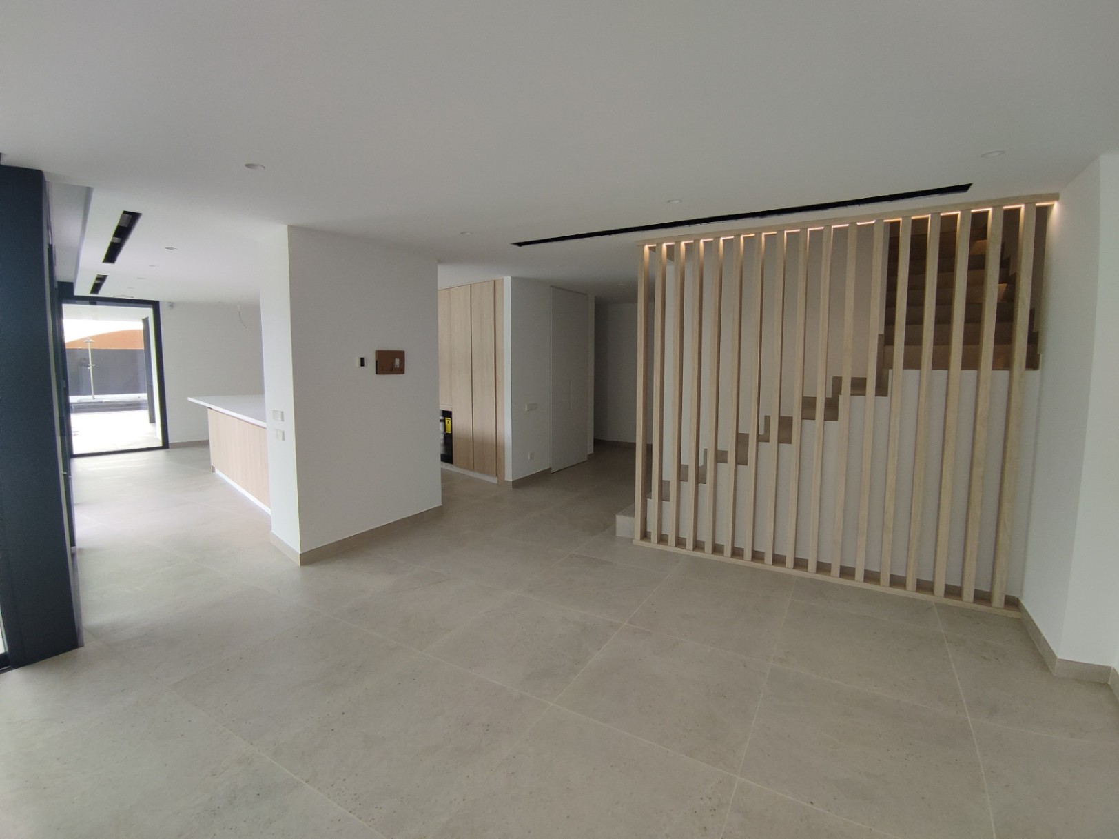 Open leefruimte met grootformaat vloertegels en een designtrap voorzien van verticale houten lamellen en subtiele LED-verlichting.
