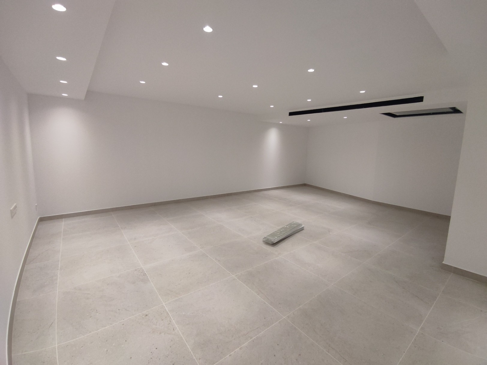 Ruime multifunctionele kamer met grootformaat porseleinen vloertegels, witte muren en geïntegreerde LED-inbouwspots in het plafond.
