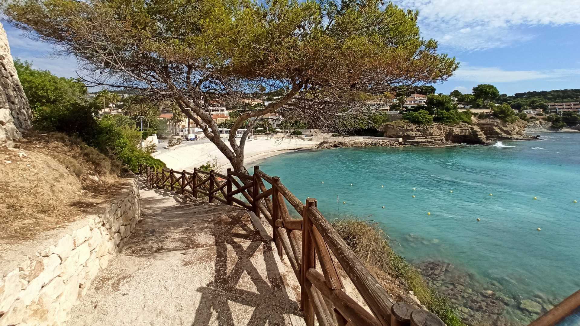Kustpad met houten omheining en natuurstenen muren, met directe toegang tot het zandstrand van La Fustera en het turquoise water van de Middellandse Zee.