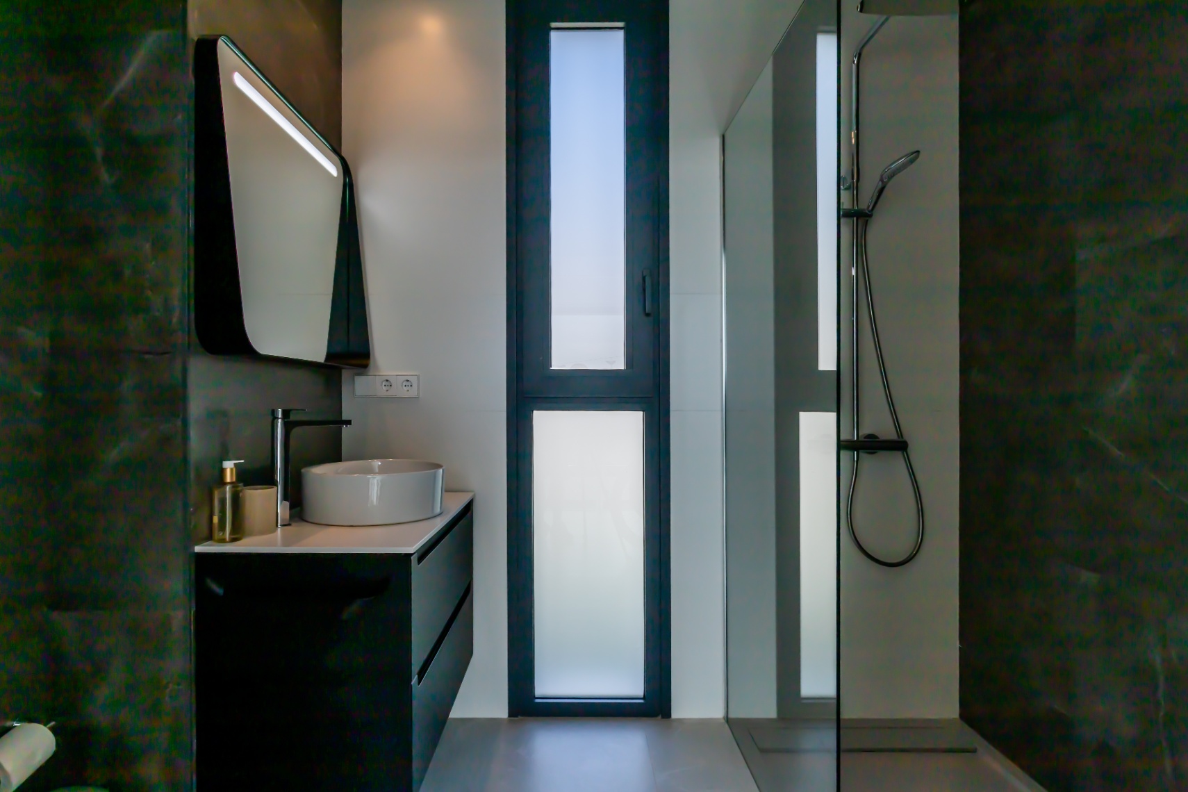 Detail van een moderne badkamer met keramische wastafel, zwart meubel en glazen douchecabine.