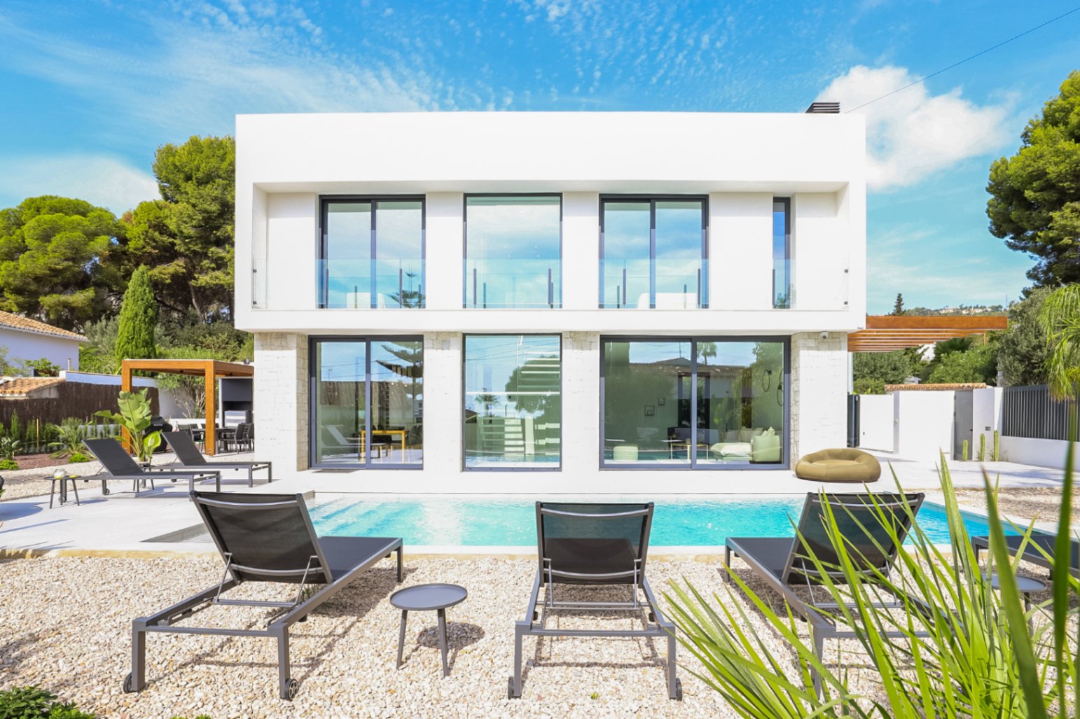 Exterieur van de villa met zwembad, ligstoelen en een stenen gevel met grote ramen.
