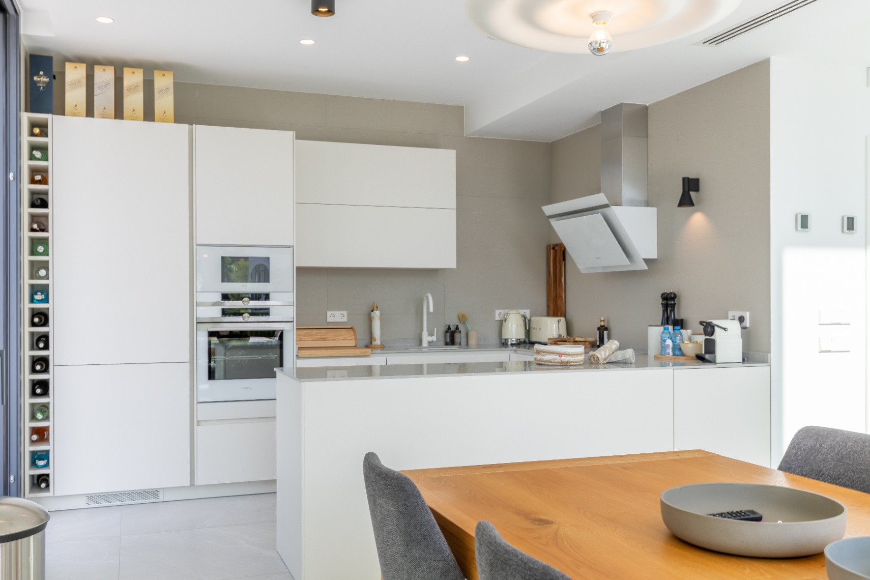 Moderne keuken met witte kasten, geïntegreerde apparatuur en een houten eettafel.