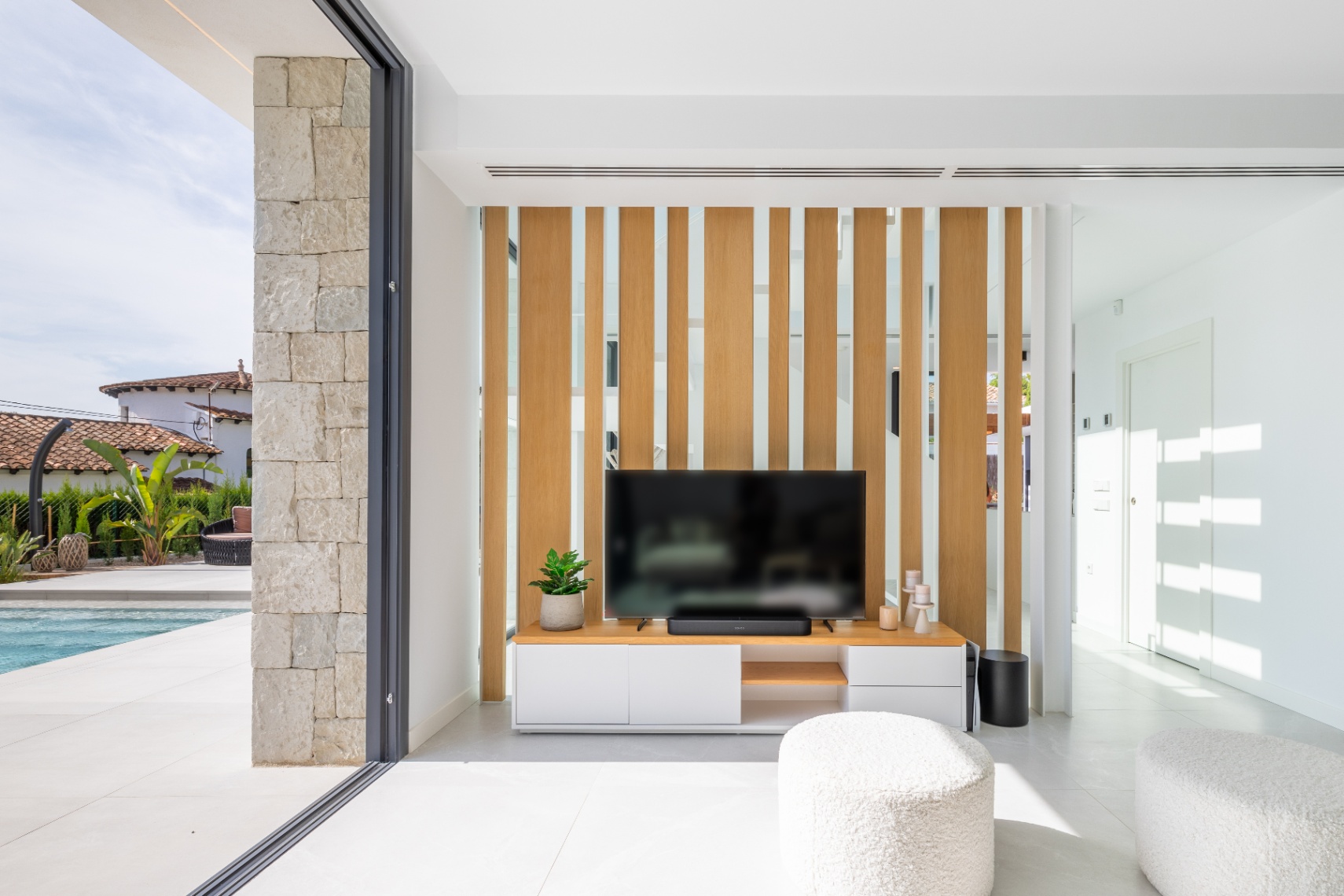 Moderne woonkamer met tv-meubel en licht houten scherm. Toegang tot het terras met zwembad.