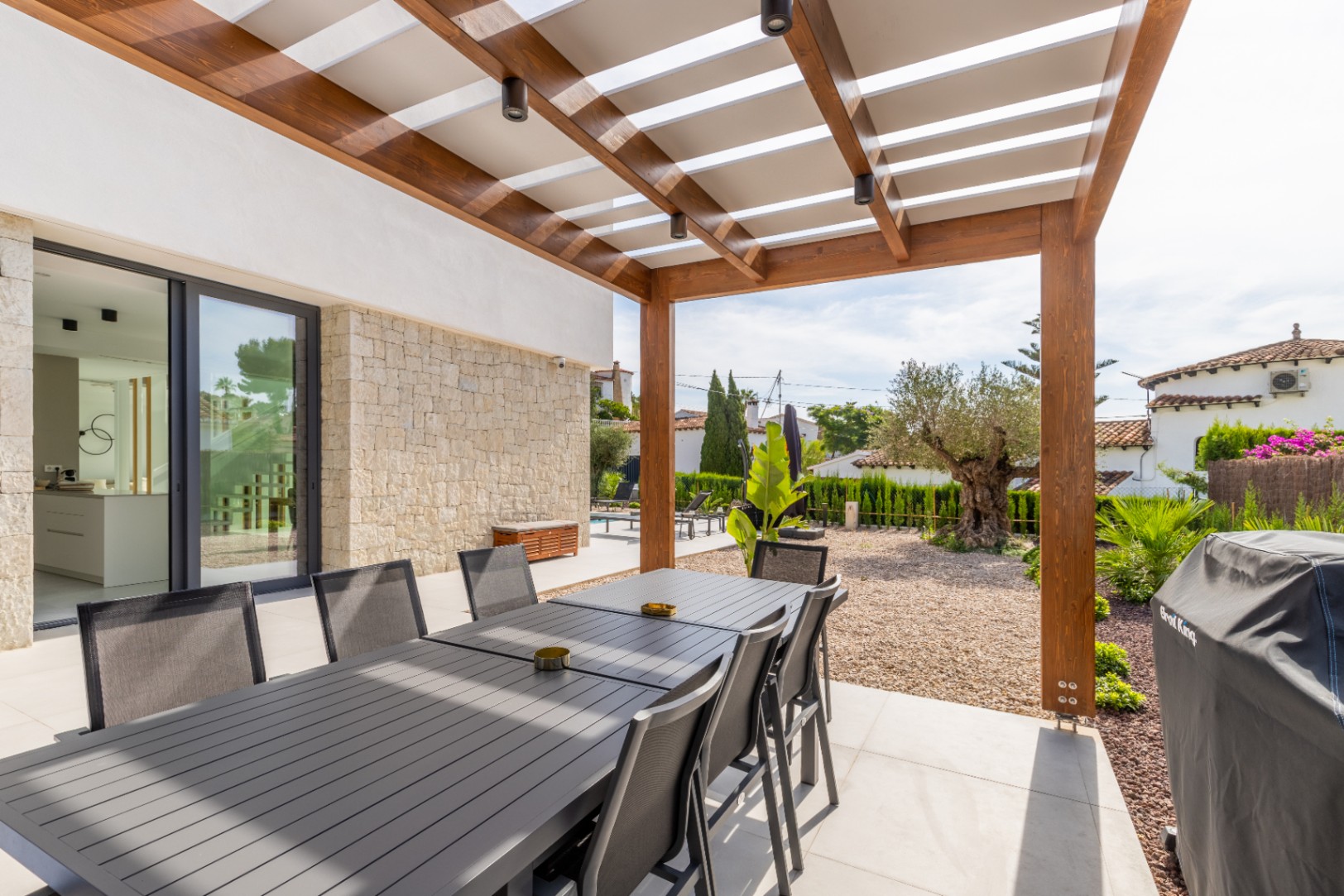 Overdekte eethoek buiten met houten pergola en uitzicht op de mediterrane tuin.