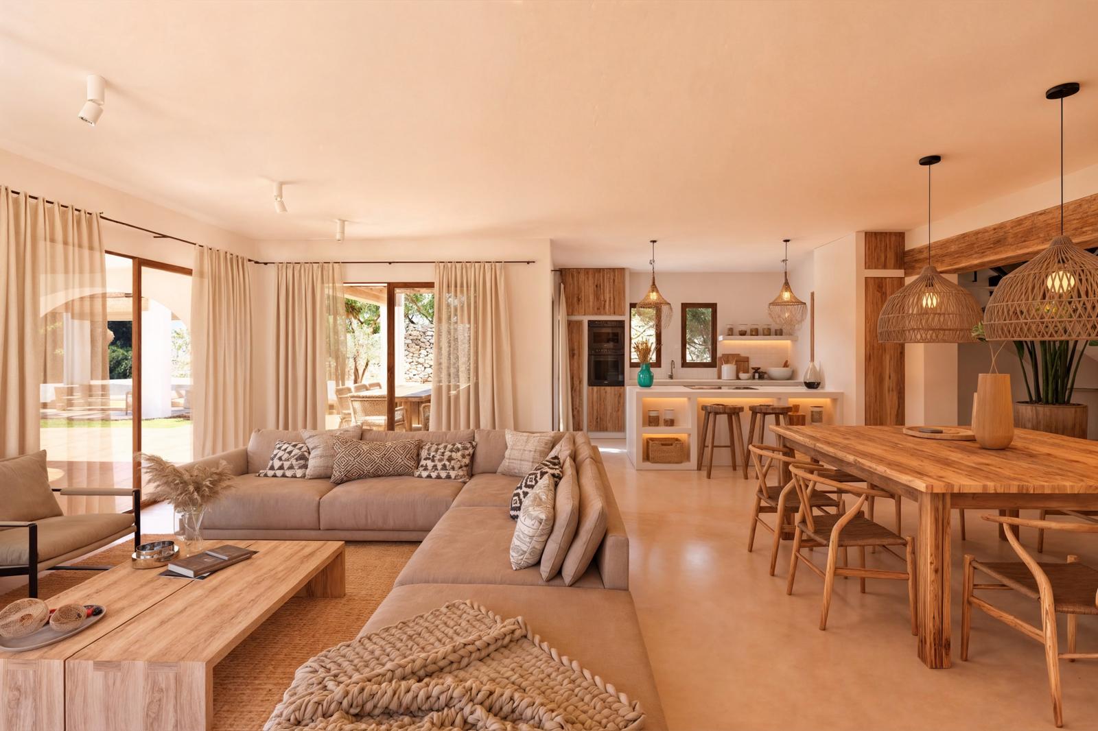Open woon- en eetkamer met natuurhouten meubels, neutrale banken en een moderne keuken met kookeiland. Grote glazen deuren en rieten hanglampen zorgen voor een lichte, rustieke sfeer.