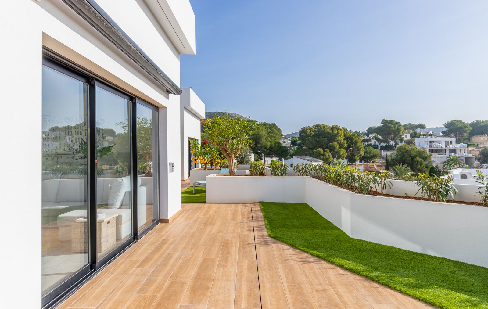 Bovenste terras met keramische houtlook vloer, kunstgrasvlakken en geïntegreerde witte plantenbakken met uitzicht op de woonwijk.