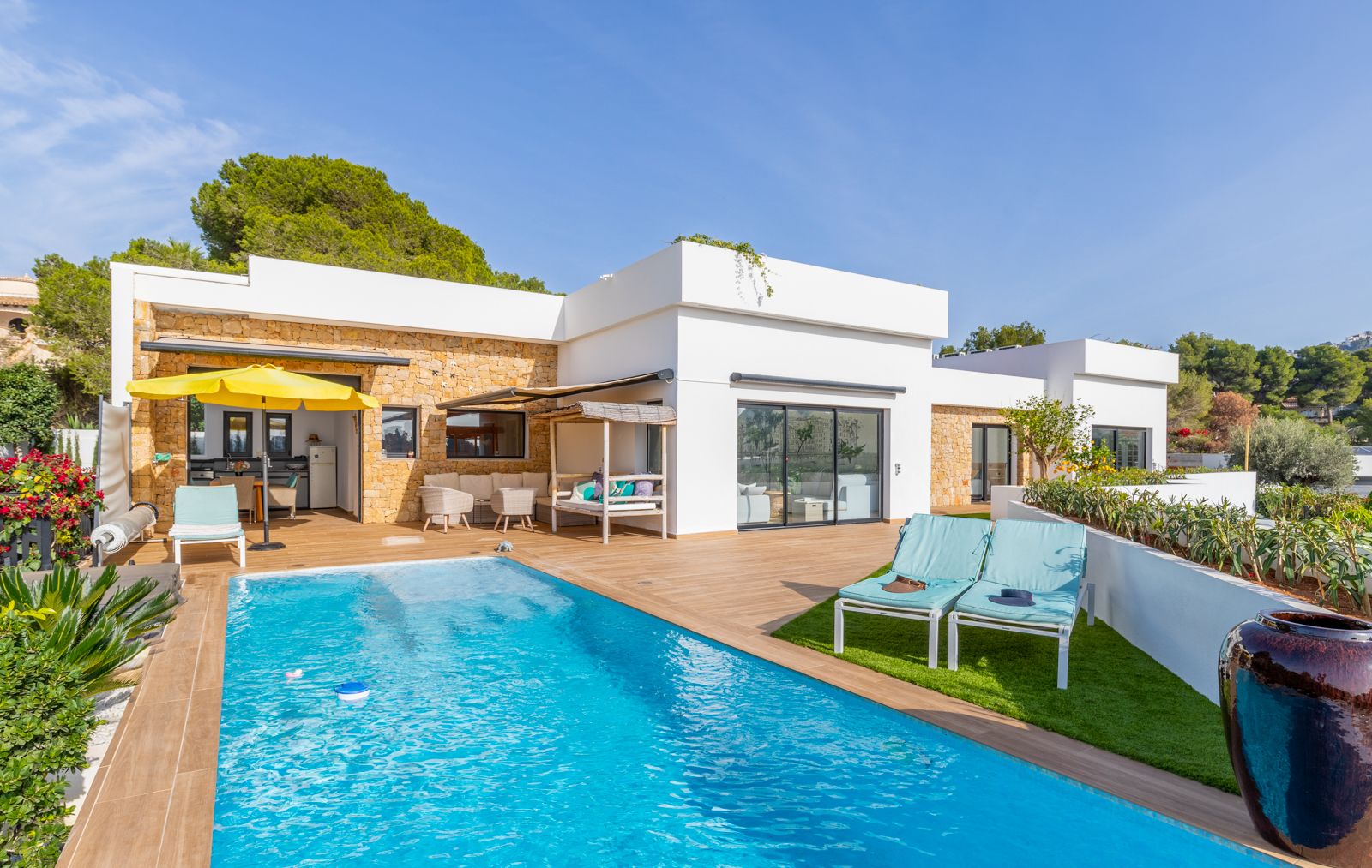 Buitenterras met zwembad, keramische houtlook tegels en natuurstenen gevels. Voorzien van een buitenkeuken, solarium met kunstgras en diverse comfortabele zithoeken.