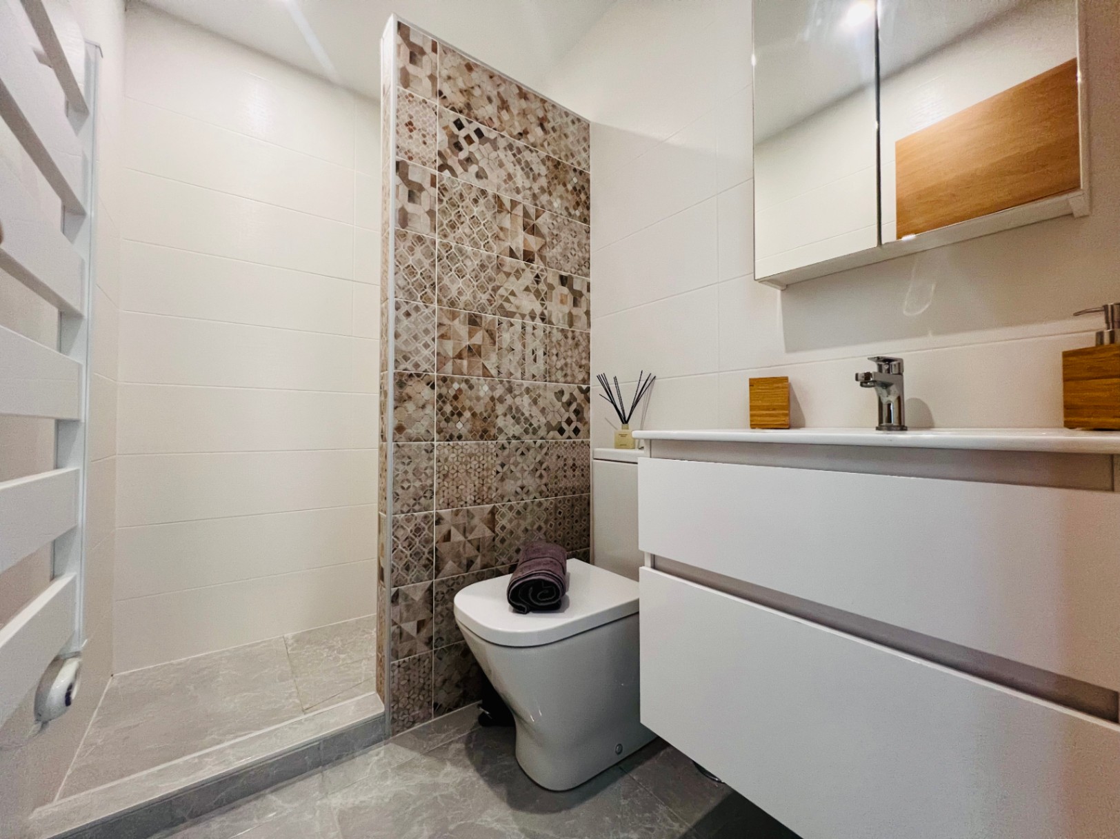 Moderne badkamer met inloopdouche, decoratieve wand met geometrische tegels, wit zwevend wastafelmeubel en een design handdoekradiator.