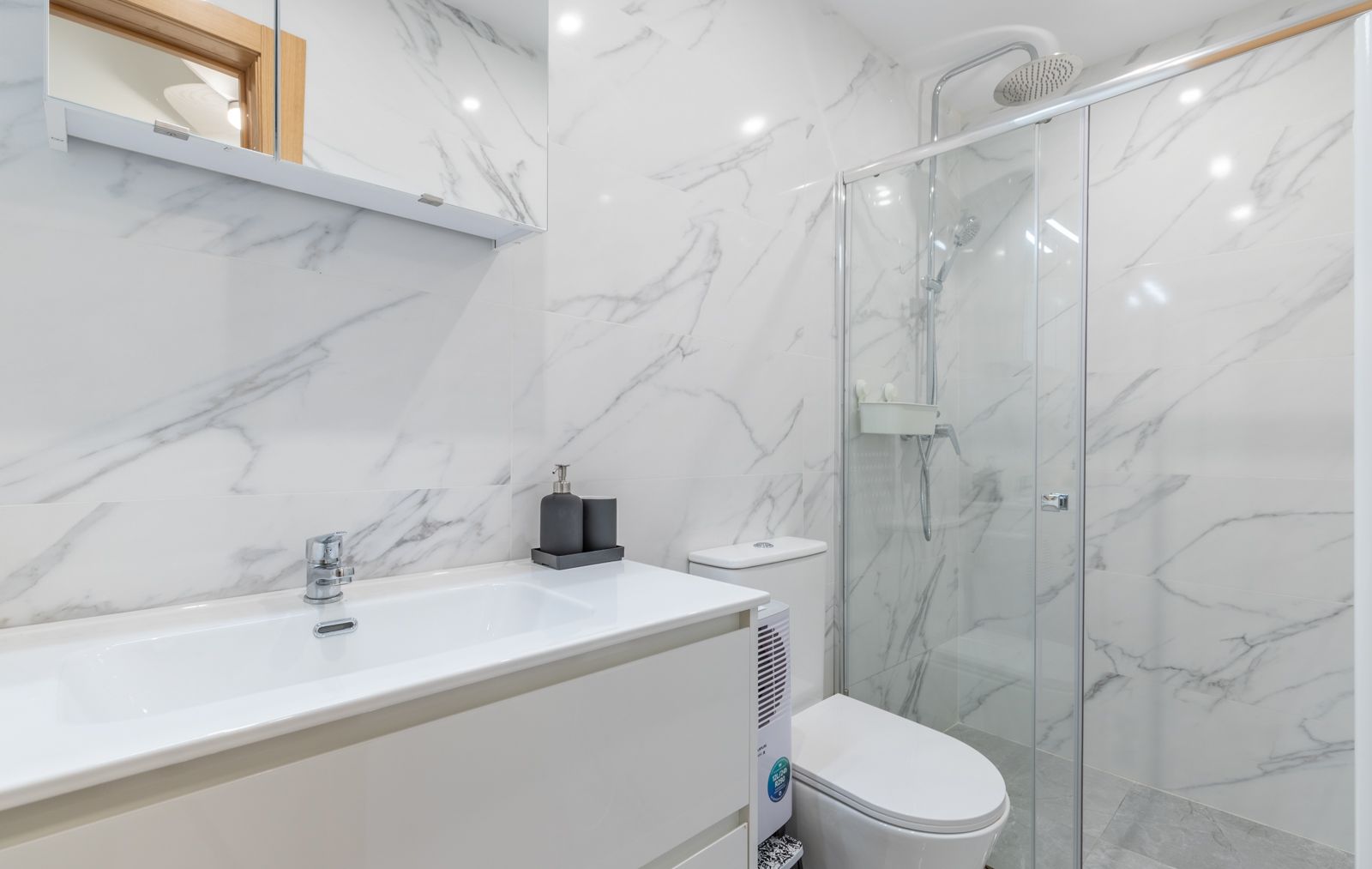 Moderne badkamer met wanden in marmerlook, een wit wastafelmeubel en een inloopdouche met glazen wand en chromen kranen.