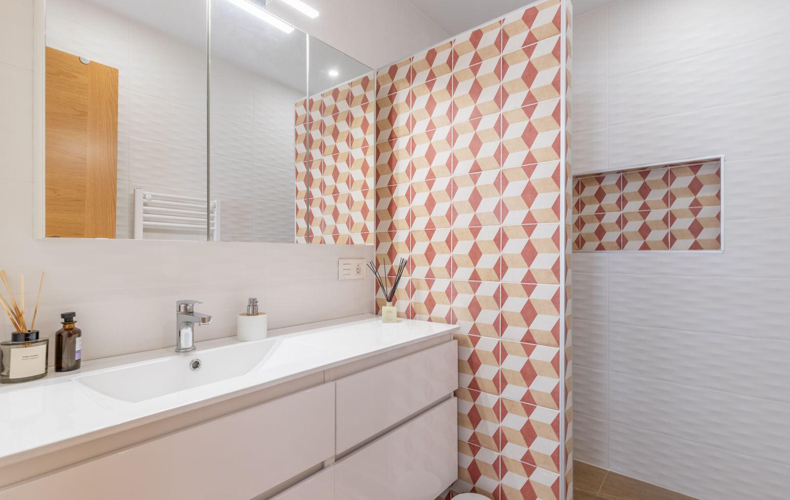 Moderne badkamer met wit wastafelmeubel, spiegelkast en een accentmuur met geometrische tegels voorzien van een ingebouwde nis.