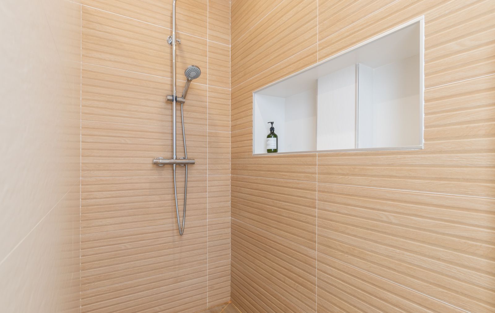 Moderne inloopdouche met horizontale houtlook tegels, chromen kranen en een praktische ingebouwde nis in de muur voor toiletartikelen.