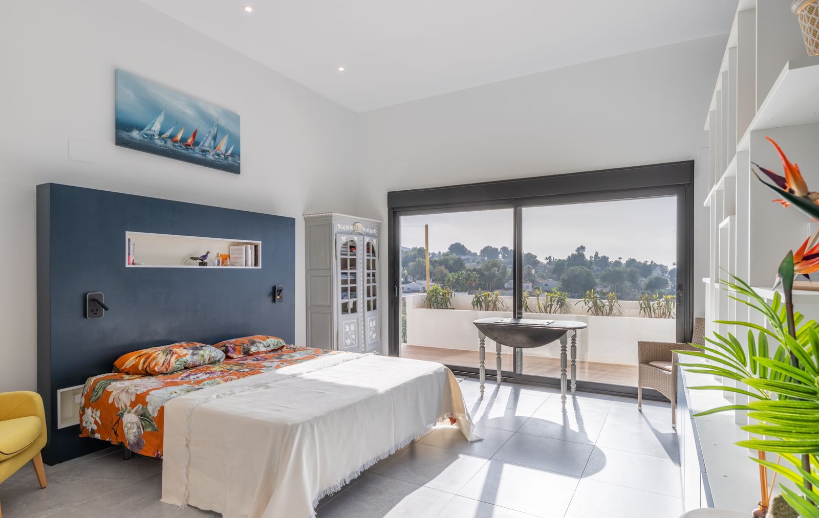 Moderne slaapkamer met een donkerblauwe accentmuur, ingebouwde nis en directe toegang tot het terras via grote glazen schuifdeuren.