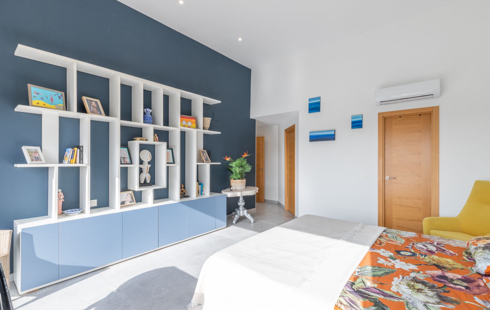 Moderne slaapkamer met een wit geometrisch wandrek tegen een marineblauwe accentmuur, geïntegreerde kasten en een lichte tegelvloer.