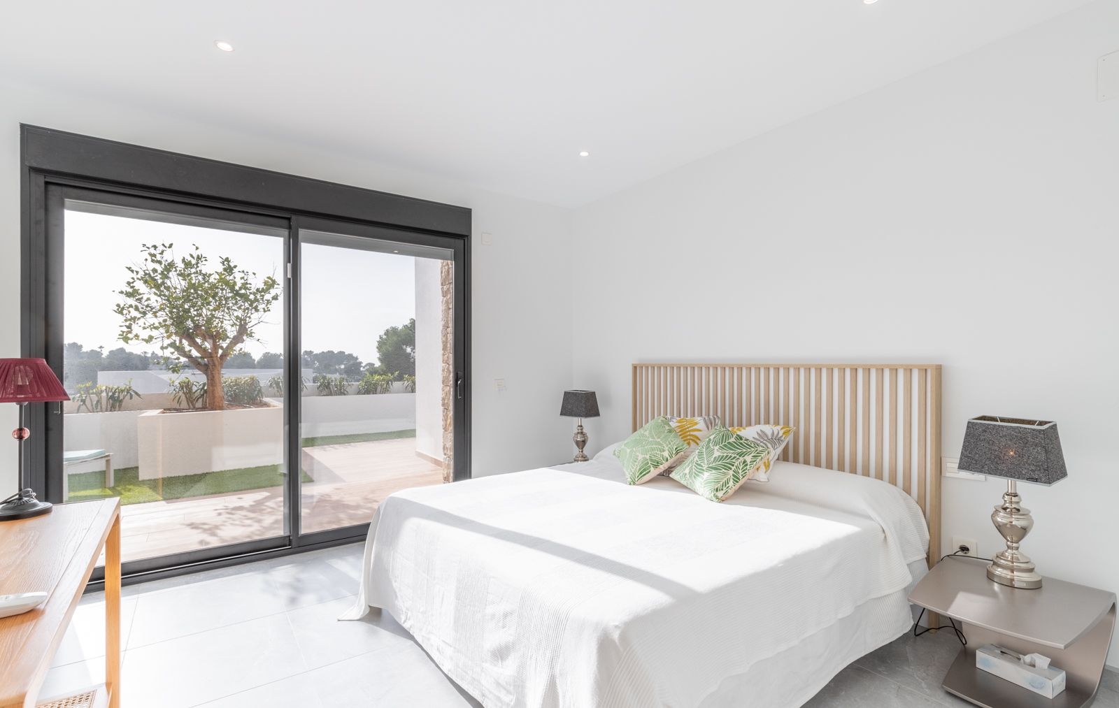 Moderne slaapkamer met houten latten hoofdbord, grote glazen schuifdeuren naar het privéterras en inbouwspots in het plafond.