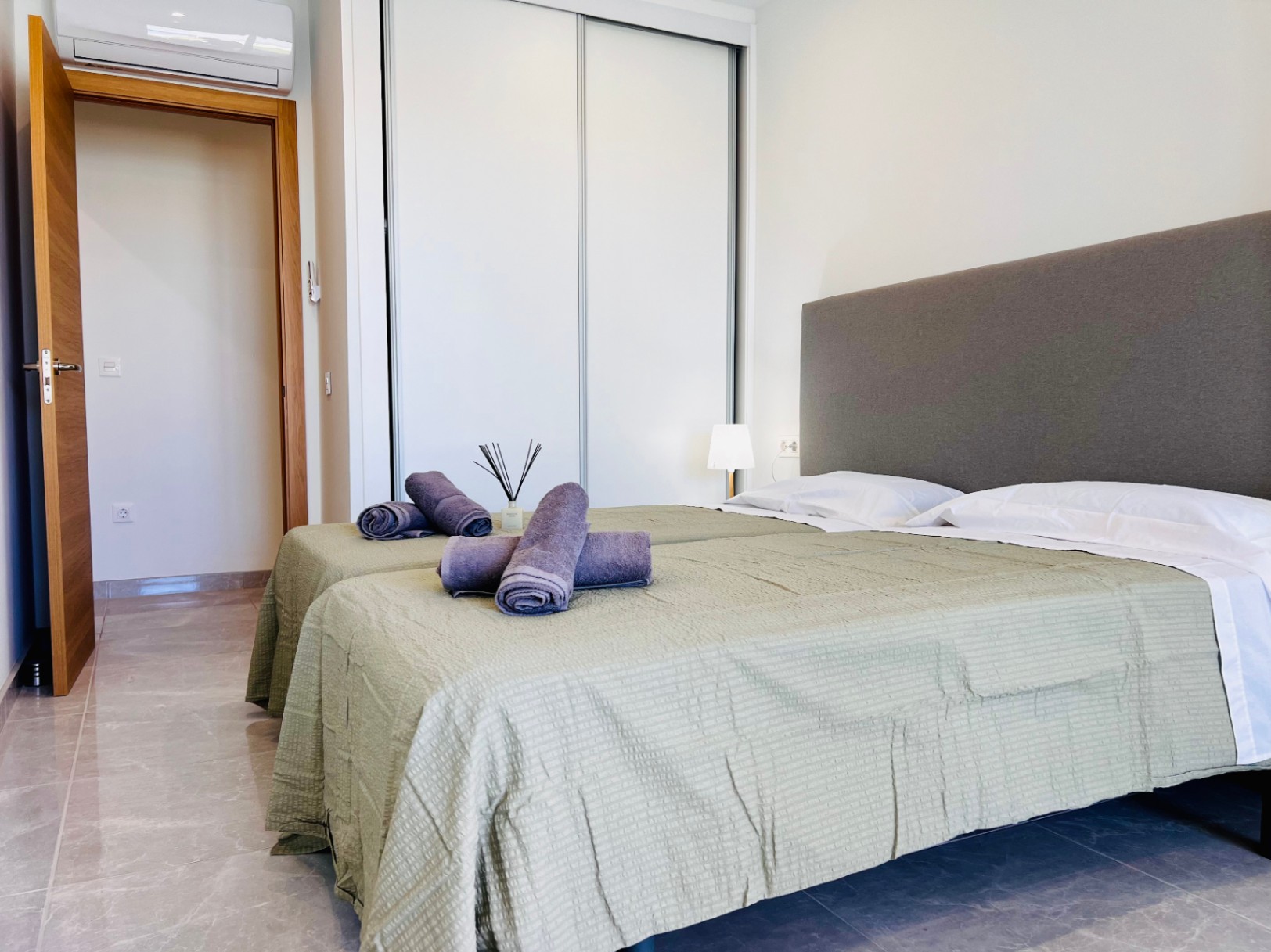 Moderne slaapkamer met witte inbouwkasten, porseleinen tegelvloer en individuele airconditioning. De binnendeuren van natuurlijk hout passen bij het strakke ontwerp.