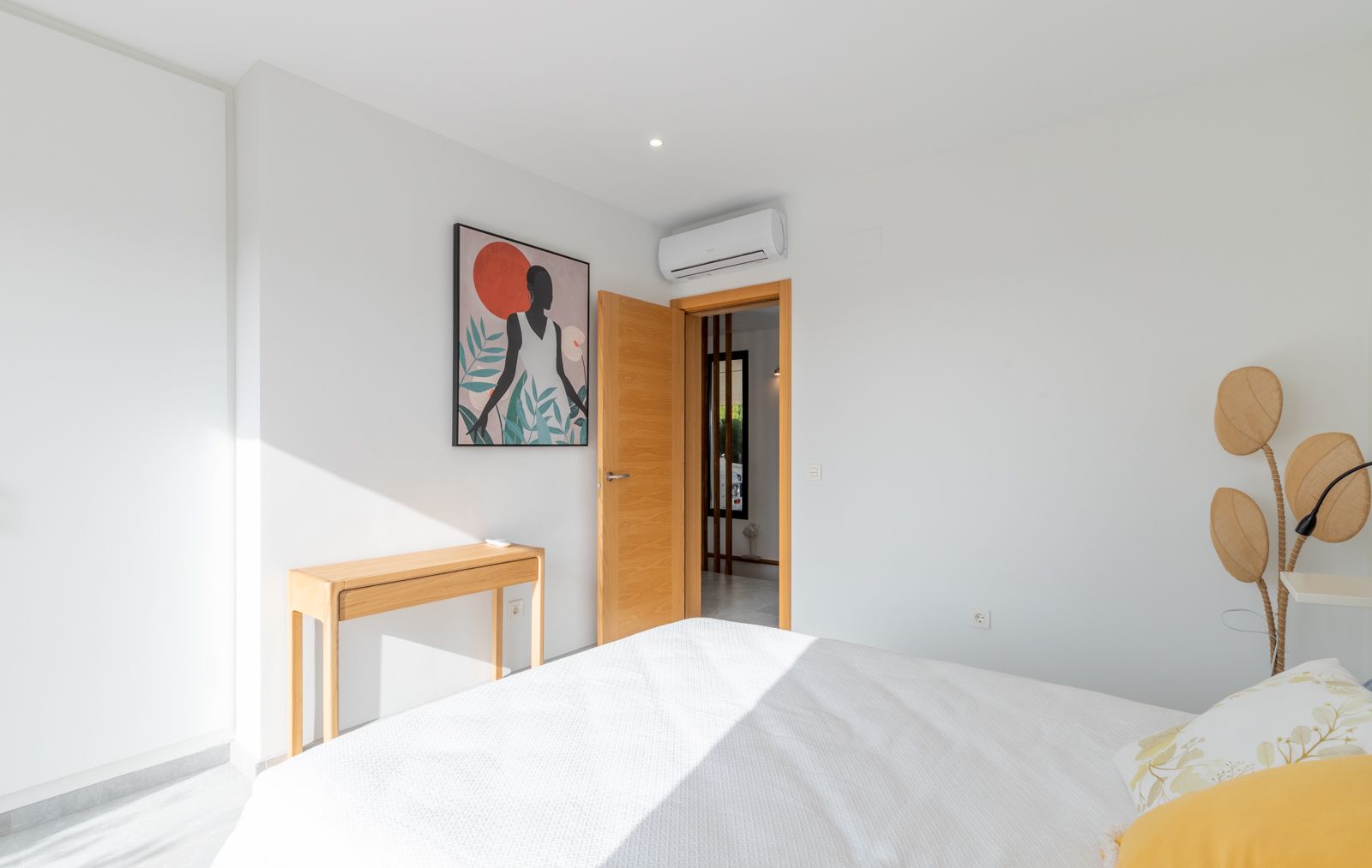Moderne slaapkamer met witte muren, een console van natuurlijk hout en split-airconditioning. De ruimte is afgewerkt met licht houten timmerwerk en eigentijdse decoratie.