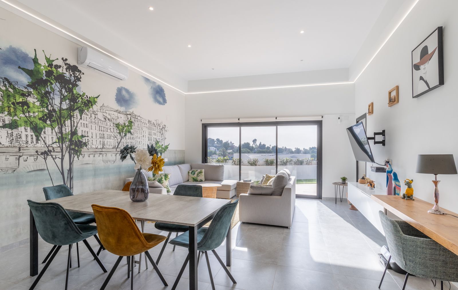 Moderne woon- en eetkamer met een artistieke muurschildering, eigentijds meubilair en grote schuifdeuren die directe toegang bieden tot het terras.