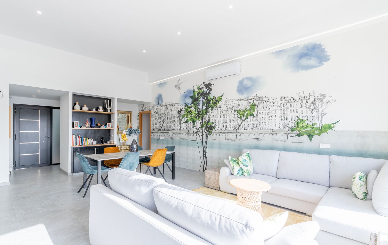 Open woon- en eetkamer met een ruime hoekbank, een artistieke muurschildering en modern meubilair onder subtiele inbouwverlichting.