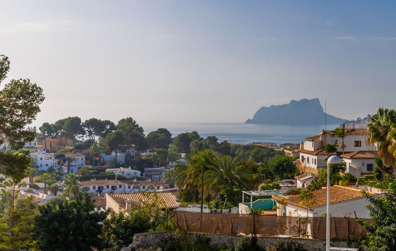Panoramisch uitzicht op de Middellandse Zee en de Peñón de Ifach, uitkijkend over witte villa's en weelderige mediterrane beplanting.