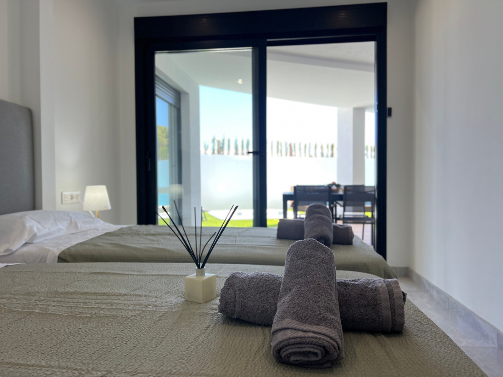Slaapkamer met twee eenpersoonsbedden en directe toegang tot het terras via grote schuifdeuren met zwarte profielen, gecombineerd met een minimalistisch interieur.