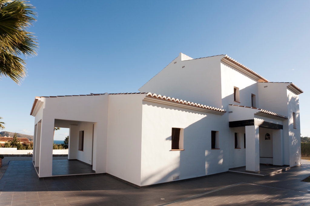 Buitenaanzicht van de mediterrane villa met witte gevels, terracotta dakpannen en ruime betegelde terrassen die leiden naar een overdekte veranda met zeezicht.