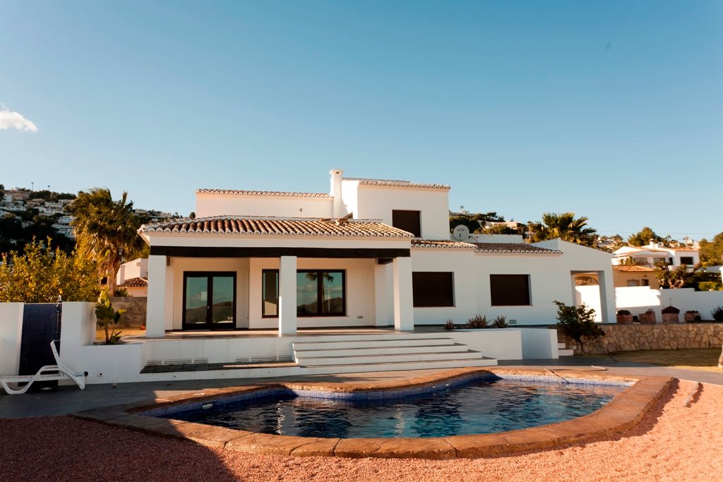 Buitenaanzicht van de villa met een niervormig zwembad, overdekt terras met donkere houten balken en een witte mediterrane architectuur.